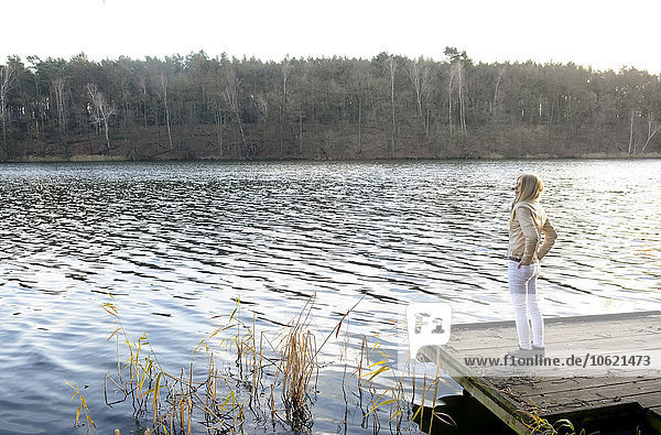 Blond woman standing on wooden boardwalk looking at a lake