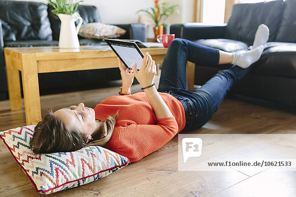 Young woman lying on the floor of her living room with digital tablet