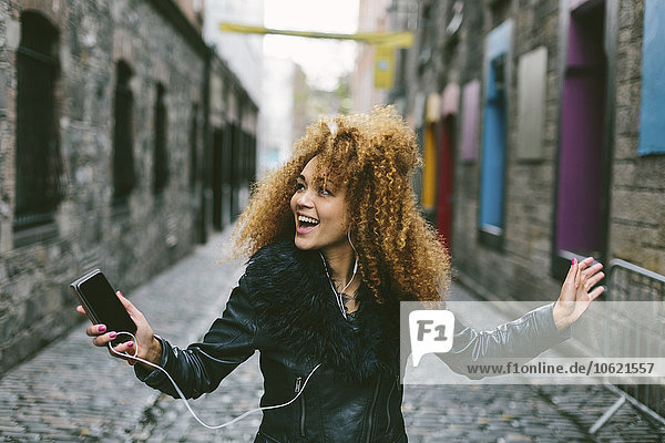 Ireland  Dublin  happy woman with afro hearing music with smartphone and earphones