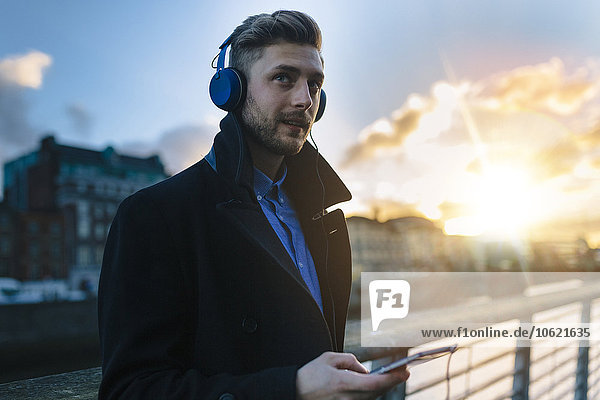 Ireland  Dublin  young man hearing music with headphones at twilight