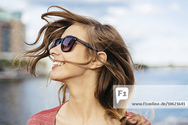 Porträt einer lächelnden Frau mit blasenden Haaren und Sonnenbrille