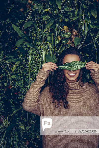 Smiling young woman covering her eyes with a leaf