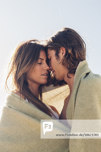 Romantic young couple together at the beach wrapped in a blanket