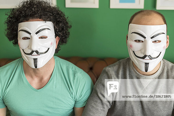 Zwei Freunde sitzen nebeneinander auf der Couch und tragen Guy Fawkes Masken.