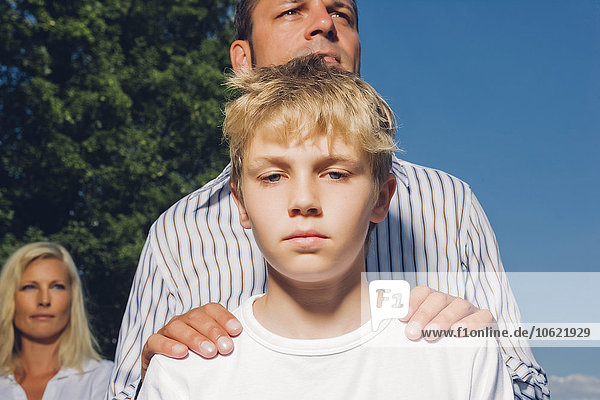 Porträt eines ernsthaft aussehenden Jungen mit seinen Eltern im Hintergrund