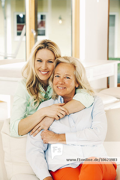 Portrait of smiling adult daughter embracing her mother on sofa