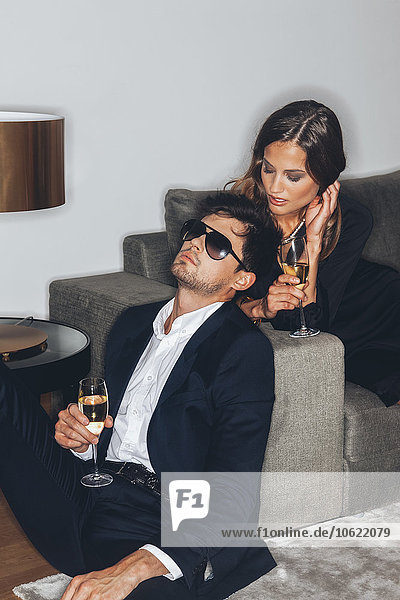 Stylish young couple with glasses of champagne at sofa