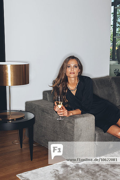 Junge Frau auf der Couch sitzend mit einem Glas Champagner