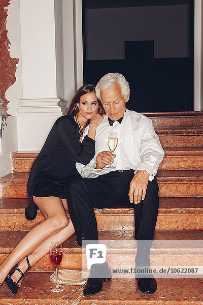 Älterer Mann und junge Frau mit Gläsern Champagner auf der Treppe