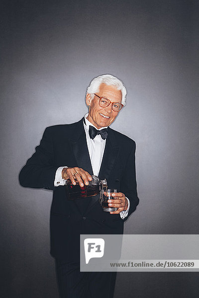 Smiling elegant senior man pouring drink into tumbler