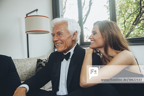 Smiling young woman with elegant senior man on couch