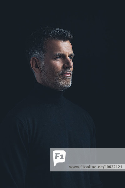 Portrait of man wearing black turtleneck in front of black background