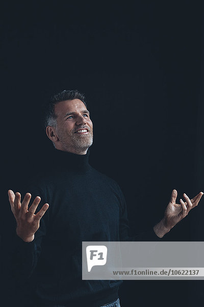 Portrait of enjoyed man wearing black turtleneck in front of black background