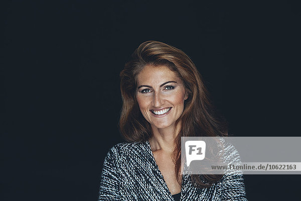 Portrait of smiling woman with brown hair in front of black background