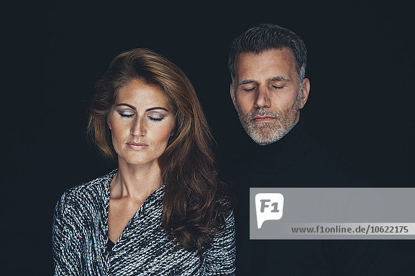 Portrait of couple with closed eyes in front of black background
