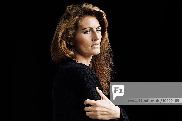 Portrait of pensive woman with brown hair in front of black background