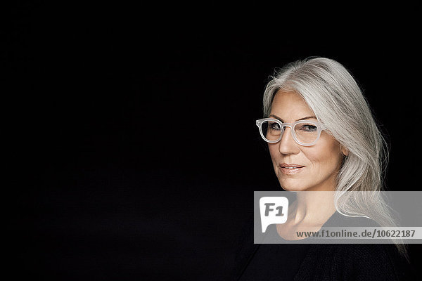 Porträt einer reifen Frau mit grauen Haaren und Brille vor schwarzem Hintergrund