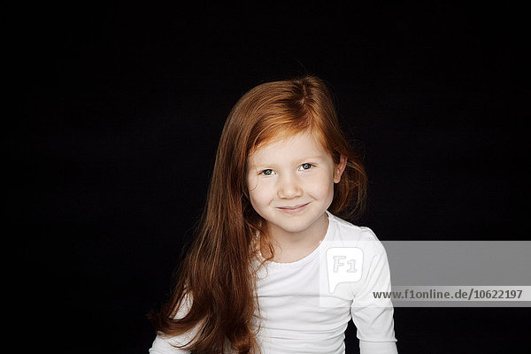 Portrait of redheaded smiling little girl in front of black background