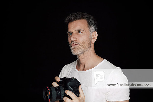 Porträt eines Mannes mit Kamera vor schwarzem Hintergrund