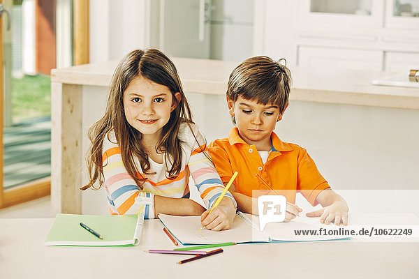 Sister and brother sitting at table with coloring book