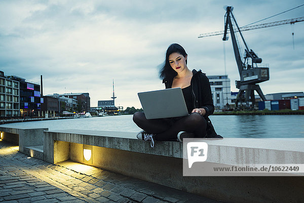 Deutschland  Münster  junge Frau mit Laptop vor dem Stadthafen sitzend