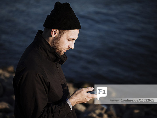 Deutschland  Köln  Mann in Herbstmode vor dem Rhein stehend mit seinem Smartphone
