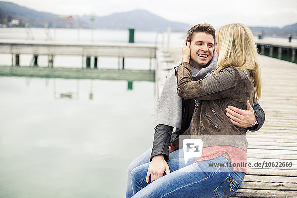Young couple kissing  sitting on boardwalk  on a lake