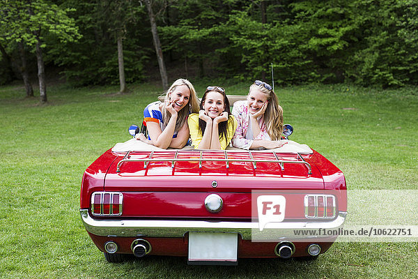 Drei glückliche junge Frauen in einem Cabriolet auf der Wiese geparkt