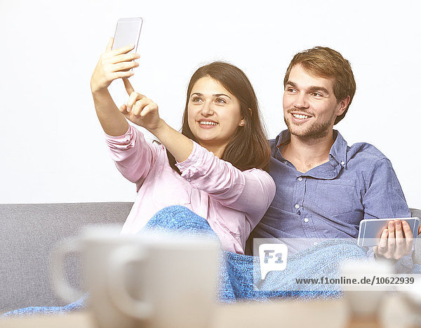 Junges Paar auf der Couch nimmt Selfie mit Handy
