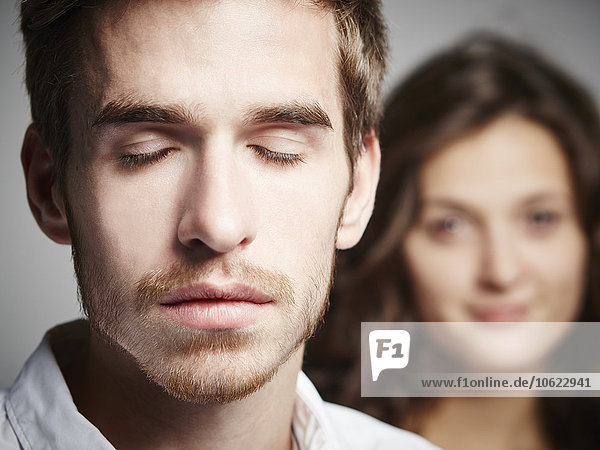 Porträt eines jungen Mannes mit geschlossenen Augen und Freundin im Hintergrund