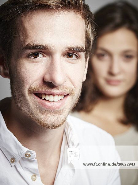 Portrait des lächelnden jungen Mannes mit Freundin im Hintergrund