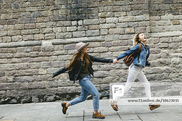 Spanien  Barcelona  zwei junge Frauen  die Hand in Hand in der Stadt laufen.