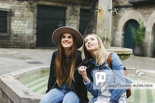 Spanien  Barcelona  zwei junge Frauen  die an einem Brunnen sitzen und nach oben schauen.