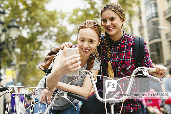 Spain  Barcelona  two young women with cell phone and bicycles in the city