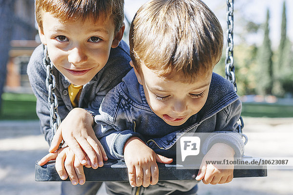 Zwei glückliche Jungs auf einer Schaukel auf dem Spielplatz