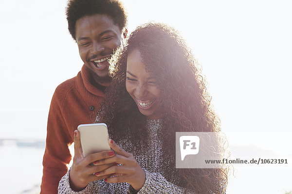 Portrait eines glücklichen jungen Paares mit Smartphone im Gegenlicht