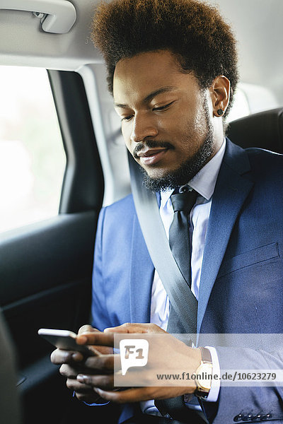 Businessman sitting on back seat of a car looking at smartphone