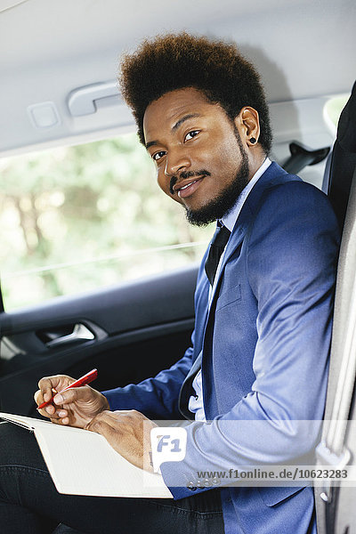 Portrait of businessman sitting on back seat of a car writing down something