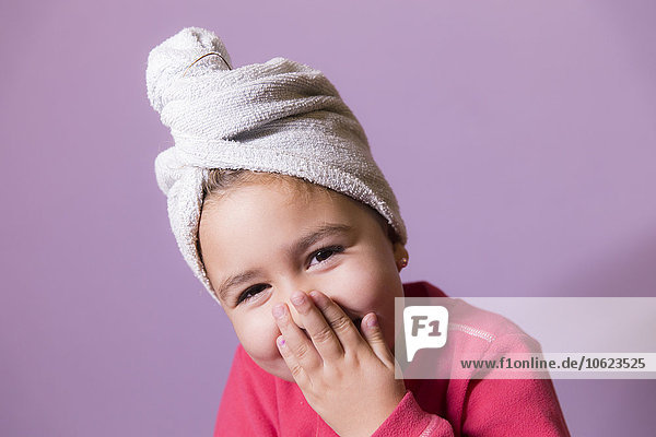 Porträt eines lachenden kleinen Mädchens,  das den Mund mit den Händen bedeckt und Handtuch-Turban trägt.