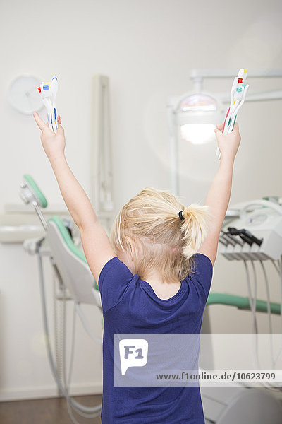 Girl in dental sugery holding toothbrushes