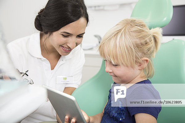 Zahnarzt und lächelndes Mädchen mit digitalem Tablett im Zahnarztstuhl