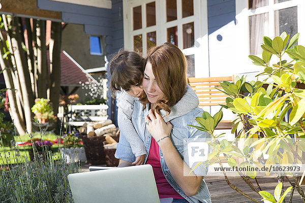 Mutter und Tochter schauen auf den Laptop auf der Gartenterrasse