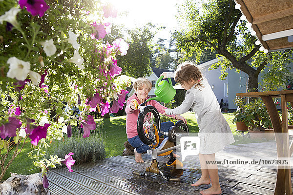Grandmother and granddaughter washing bicycle on garden terrace