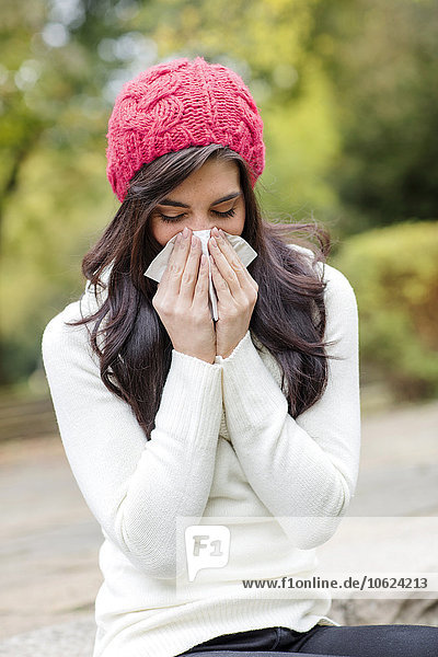 Young woman wearing red woolly hat blowing her nose