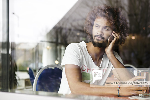 Porträt eines nachdenklichen Mannes  der in einem Café sitzt und mit einem Smartphone telefoniert.