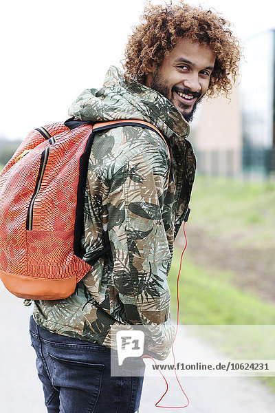 Porträt eines Mannes mit gefärbten Ringeln in Camouflage-Jacke und Rucksack über die Schulter schauend