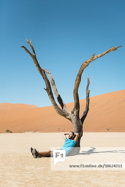 Namibia  Namib Wüste  Mann ruht am toten Baum in Deadvlei