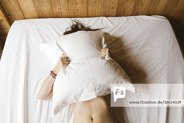 Frau  die auf dem Bett liegt und ihr Gesicht mit einem Kissen bedeckt.