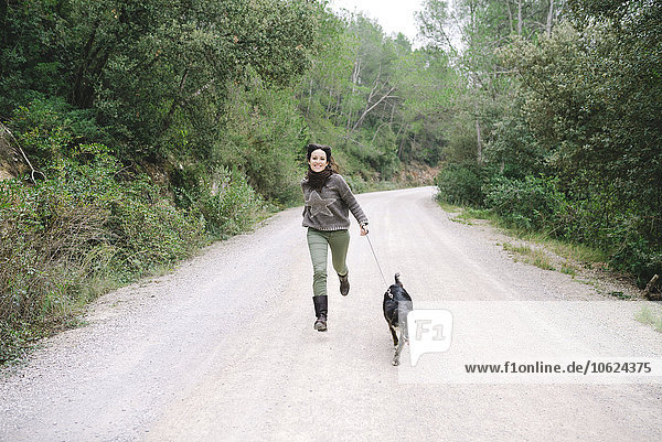 Lächelnde Frau rennt mit ihrem Hund auf einer Bergstraße