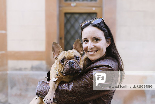 Porträt der französischen Bulldogge auf den Armen einer lächelnden jungen Frau